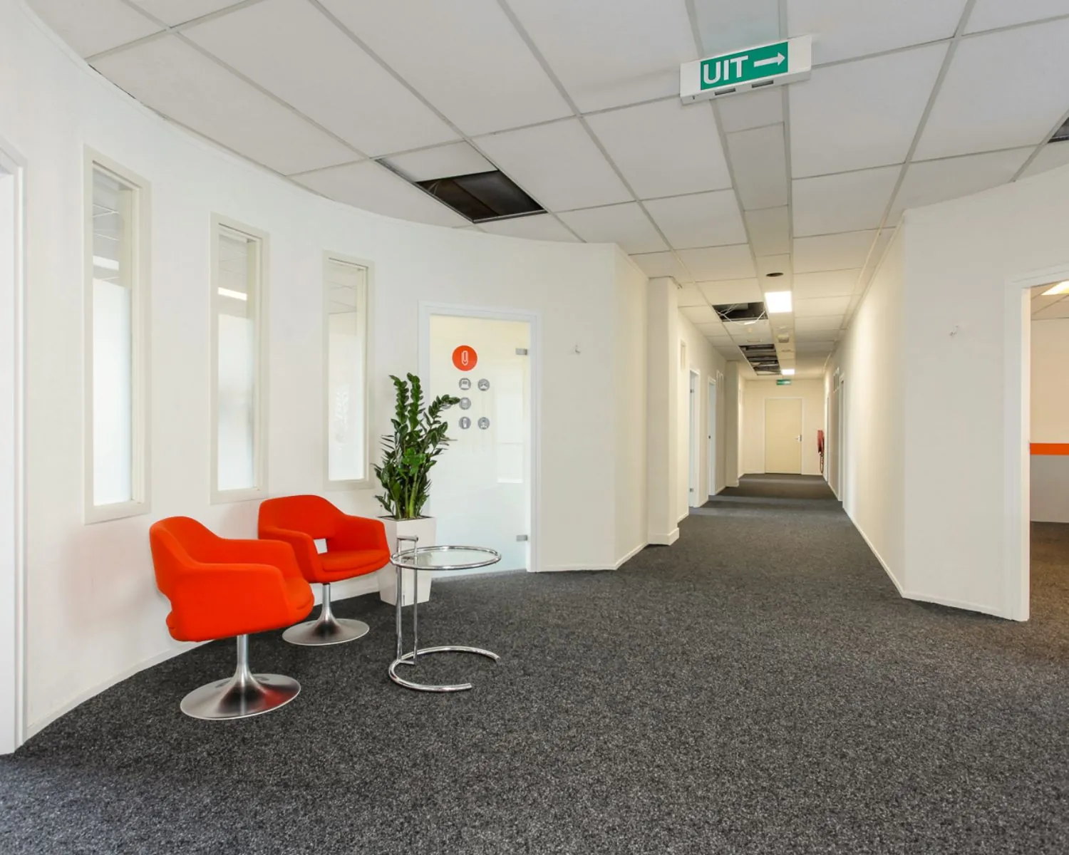 Moderne kantoorhal in De Limiet 15 in Vianen met feloranje stoelen, glazen bijzettafel en een plant.