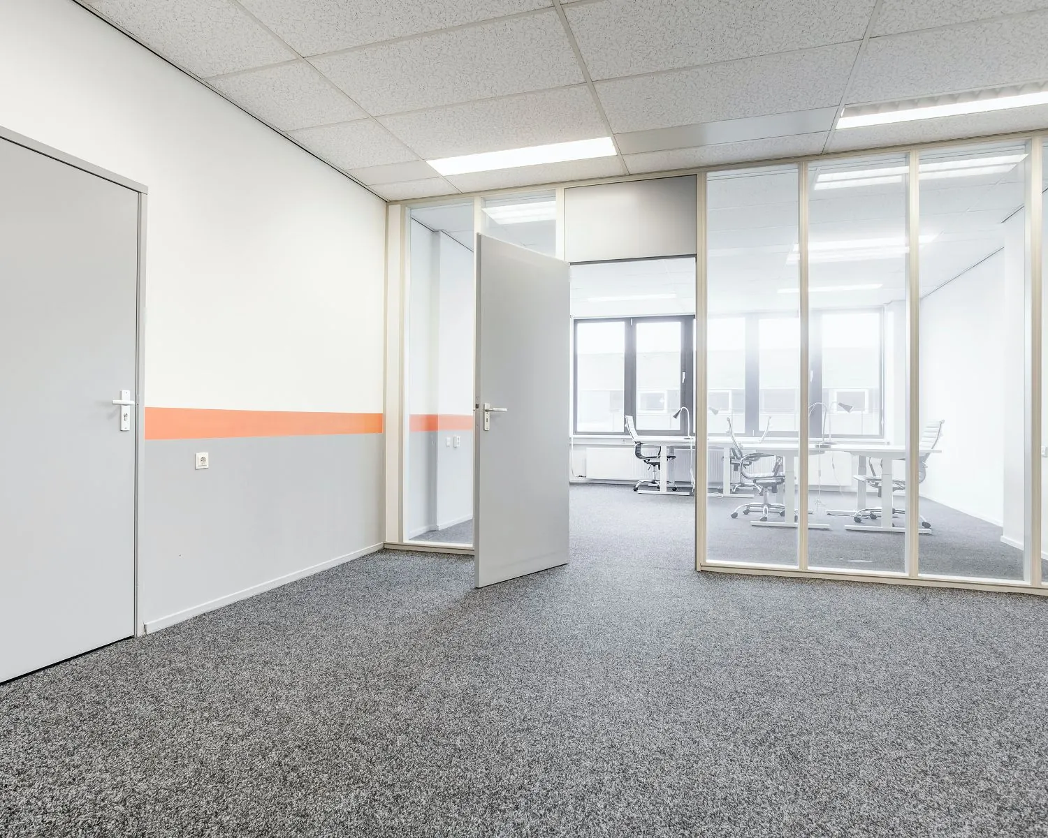 Moderne kantoorruimte in Vianen met grijze vloerbedekking, glazen scheidingswand en zicht op vergaderruimte.