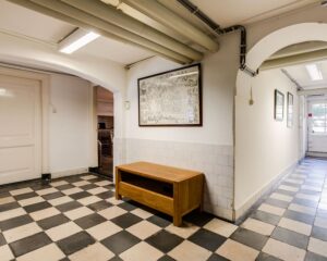 Hal van kantoorruimte aan de Dreef 36 in Haarlem met zwart-wit geblokte tegelvloer, houten tafeltje en wanddecoratie.