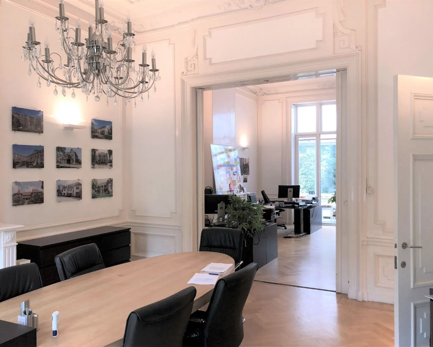 Smaakvol ingerichte kantoorruimte aan de Dreef 36 in Haarlem met vergadertafel, kroonluchter en zicht op een werkruimte met bureaus en grote ramen.