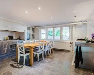 Ruime, lichte kantoorkeuken met een lange houten eettafel, acht stoelen en roestvrijstalen apparatuur in Dreef 36, Haarlem.