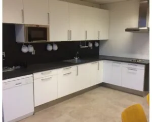 Moderne kantoorkeuken met witte kasten, zwarte werkbladen en ingebouwde apparatuur aan de Essebaan 13.