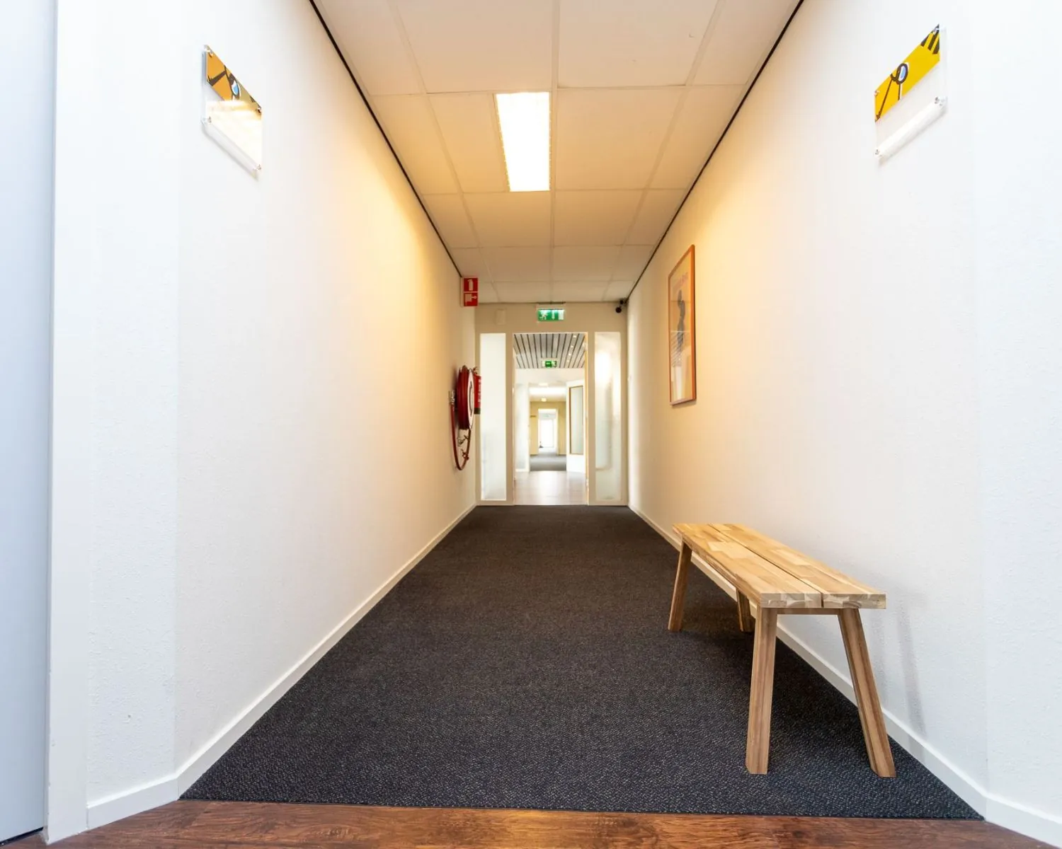 Verlichte gang in een kantoorpand aan de Fruitweg met houten bankje en brandhaspel aan de muur.