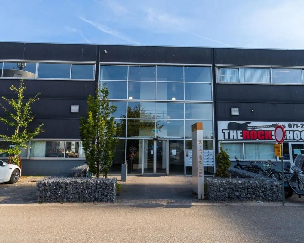 Vooraanzicht van een modern kantoorgebouw aan de Fruitweg 36-60 met glazen entree en naastgelegen muziekschool.