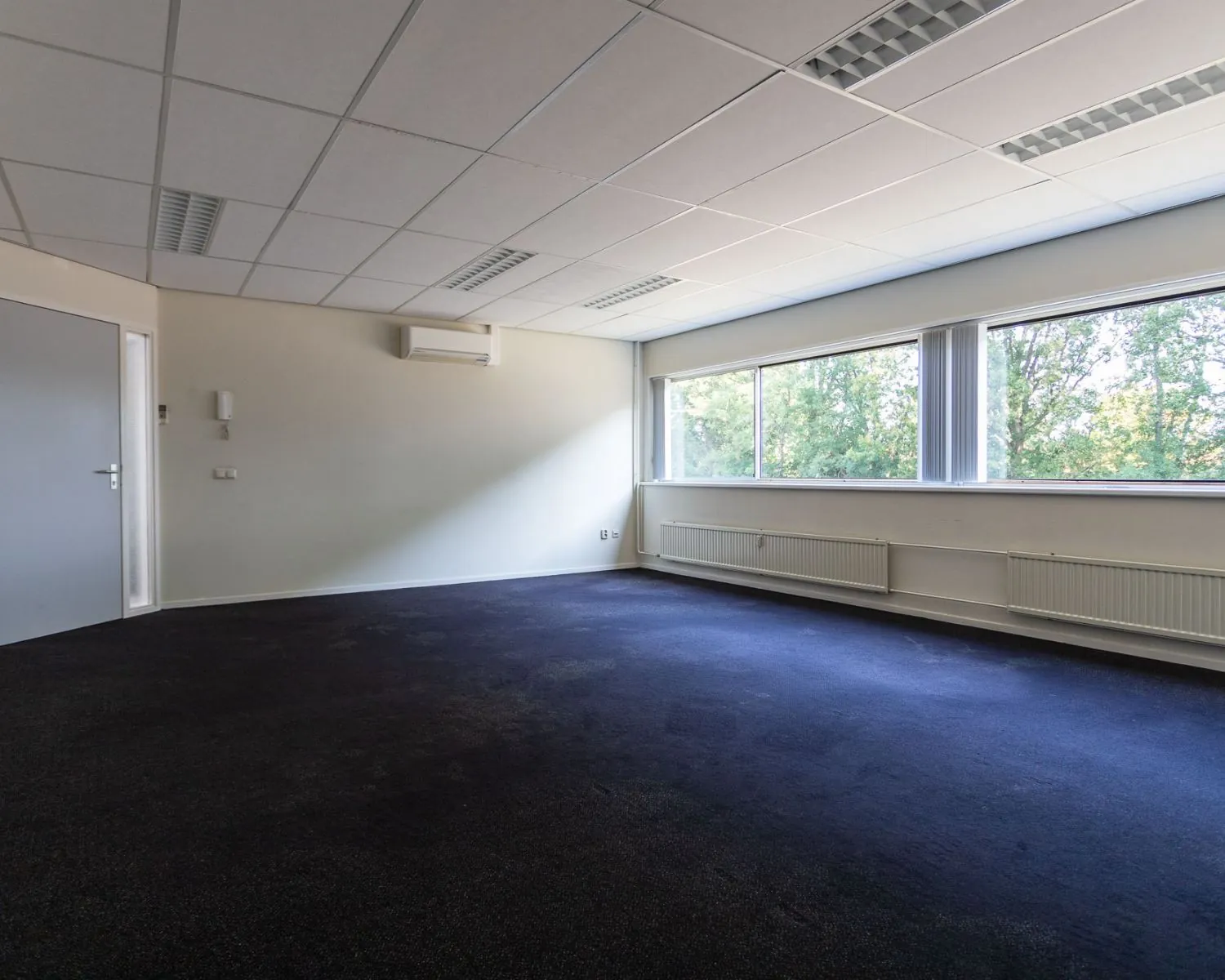 Leegstaande kantoorruimte met grote ramen en donker tapijt aan de Fruitweg 36-60.