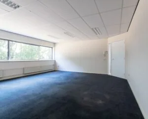 Lichte, lege kantoorruimte met donkerblauwe vloerbedekking en grote ramen aan de Fruitweg 36-60.