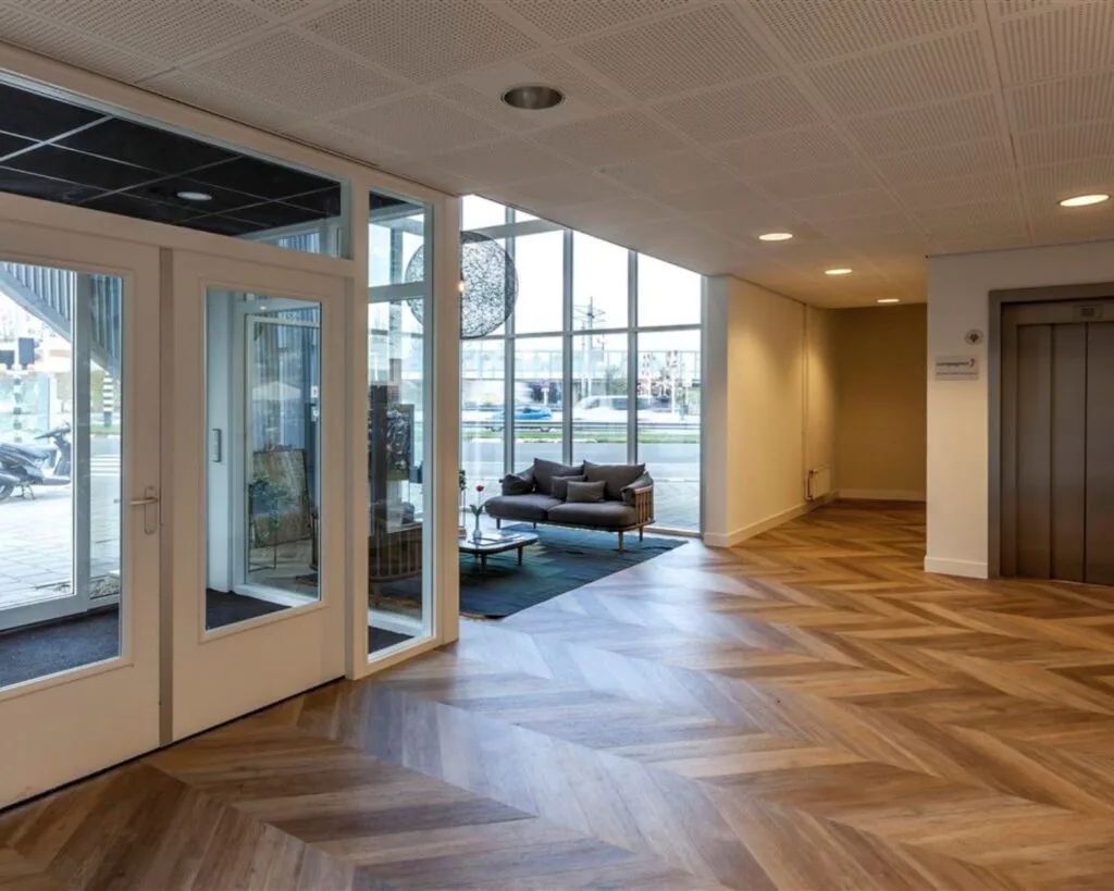 Moderne en lichte entreehal van een kantoorruimte aan de Groeneweg 2 met zitgedeelte, lift en glazen deuren.