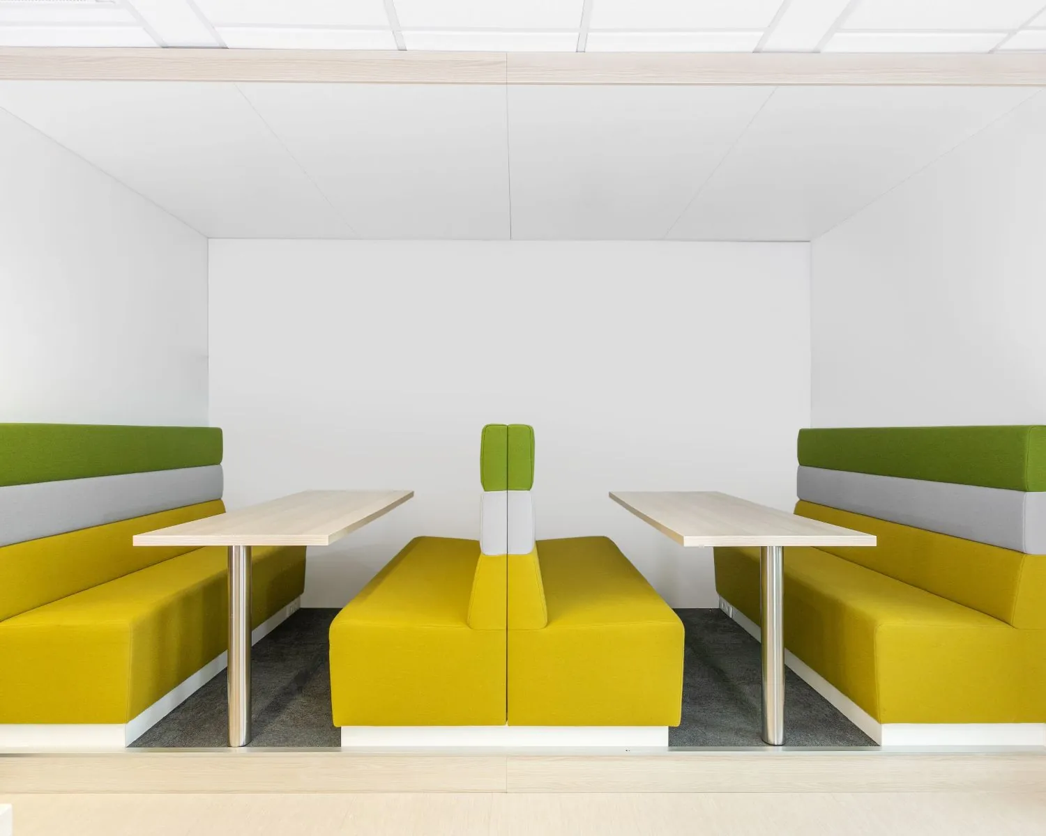 Moderne kantoorruimte met twee tegenover elkaar geplaatste zitjes met gele, grijze en groene bekleding en houten tafels in Zwolle, Grote Voort 293a.