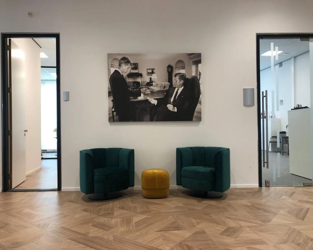 Moderne wachtruimte in een kantoor aan de Wenckebachweg 123 in Amsterdam, met twee groene fauteuils, een gele poef en een zwart-wit foto aan de muur.