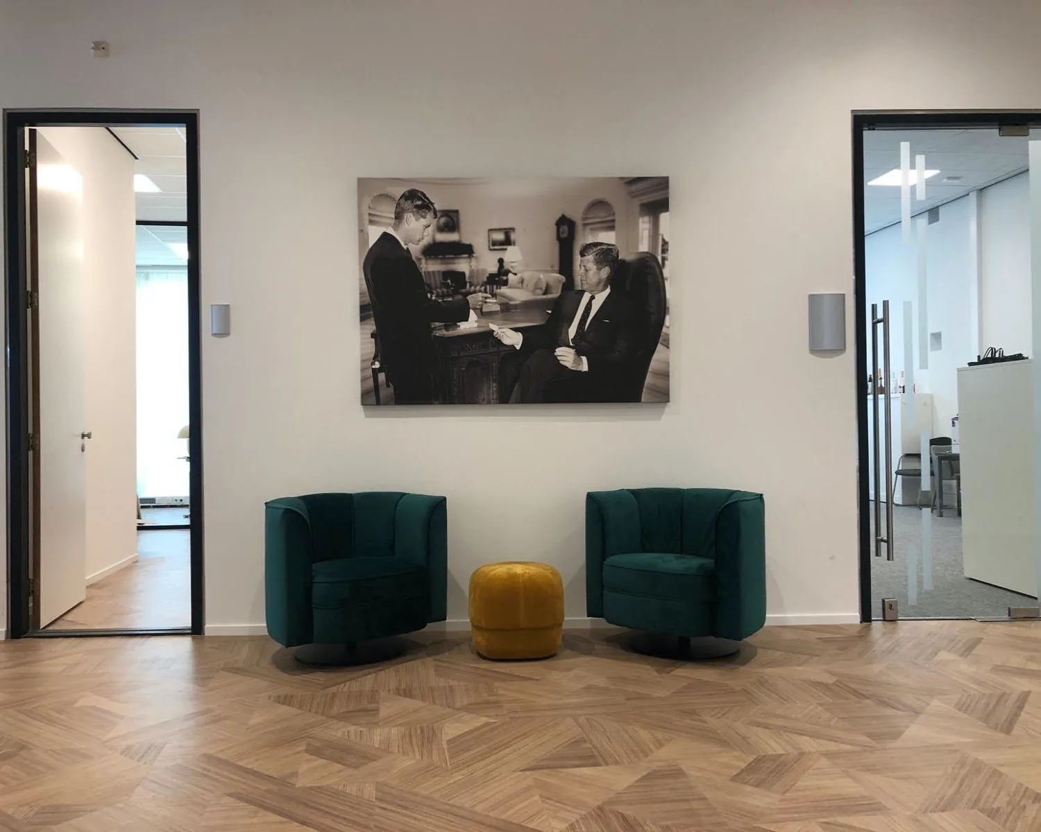 Moderne wachtruimte in een kantoor aan de Wenckebachweg 123 in Amsterdam, met twee groene fauteuils, een gele poef en een zwart-wit foto aan de muur.