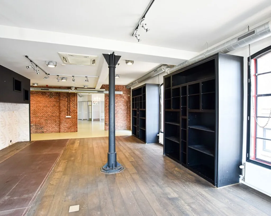 Ruime kantoorruimte te huur aan de Haarlemmerstraatweg 11 in Halfweg met houten vloer, bakstenen muur en zwarte open kasten.