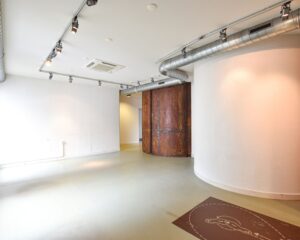Moderne, industriële kantoorruimte te huur aan de Haarlemmerstraatweg 11 in Halfweg met witte muren, zichtbare ventilatiebuizen en een roestkleurige scheidingswand.