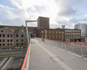 Voetgangsbrug richting kantoorpand aan de Haarlemmerstraatweg 11 in Halfweg met omliggende industriële en moderne gebouwen.