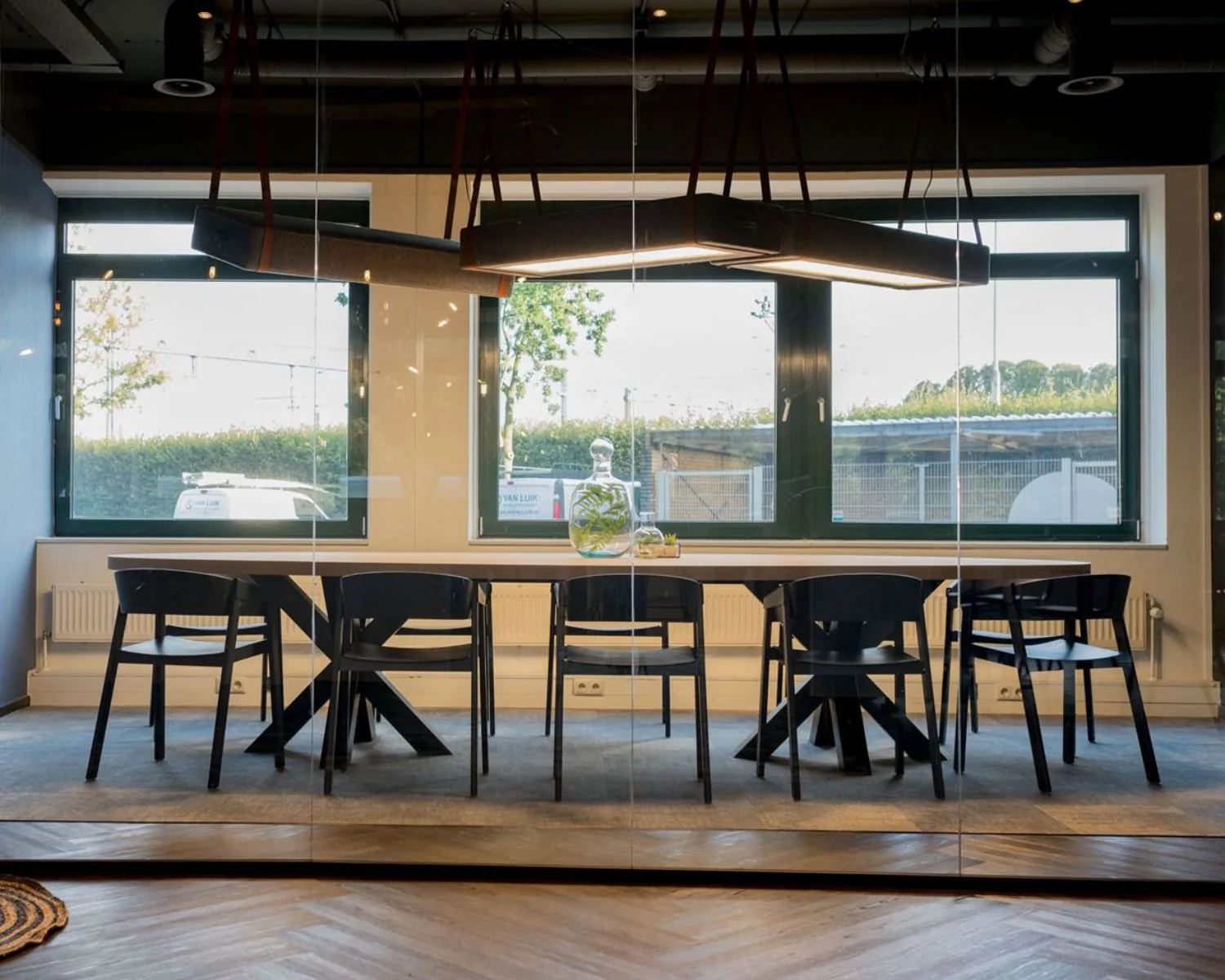 Moderne vergaderruimte met glazen wand, grote tafel, zwarte stoelen en uitzicht op buiten bij Hanzelaan 351 in Zwolle.