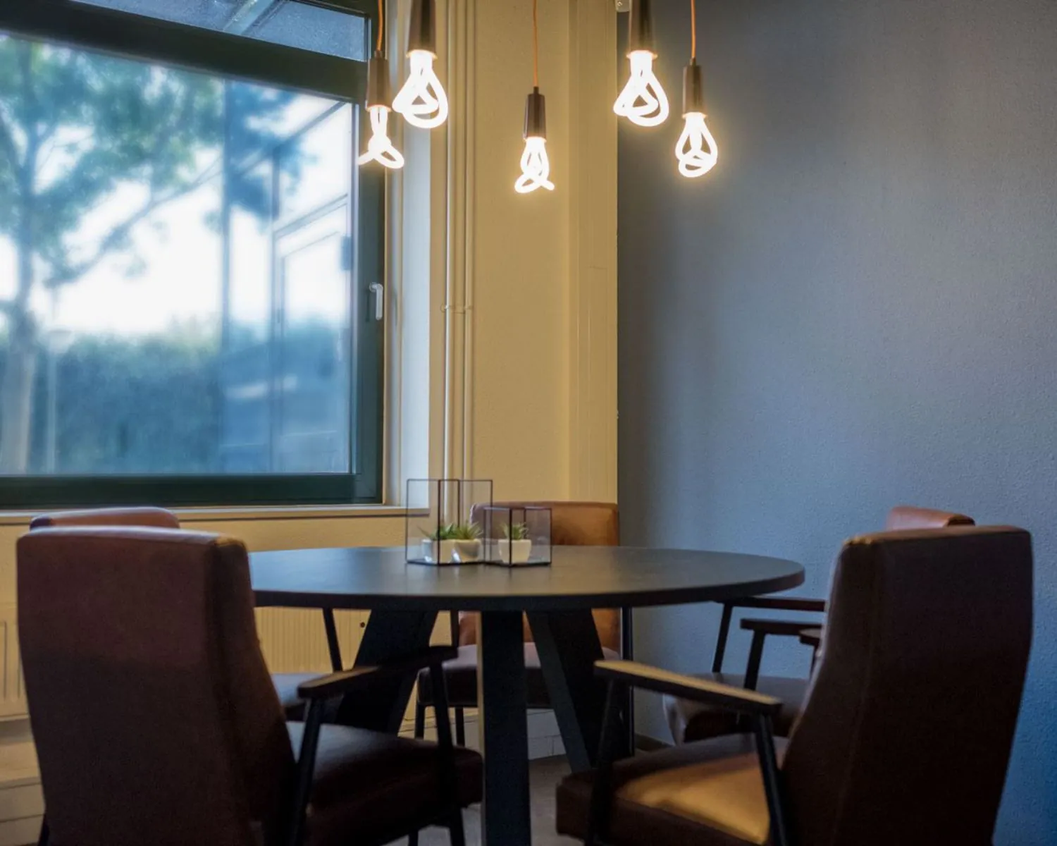 Vergaderruimte met ronde tafel, vier bruine stoelen en moderne hanglampen in kantoor aan de Hanzelaan 351 in Zwolle.