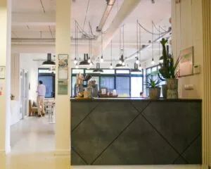 Moderne kantoorruimte aan de Hogehilweg 19 in Amsterdam met een receptiebalie, hanglampen en planten.