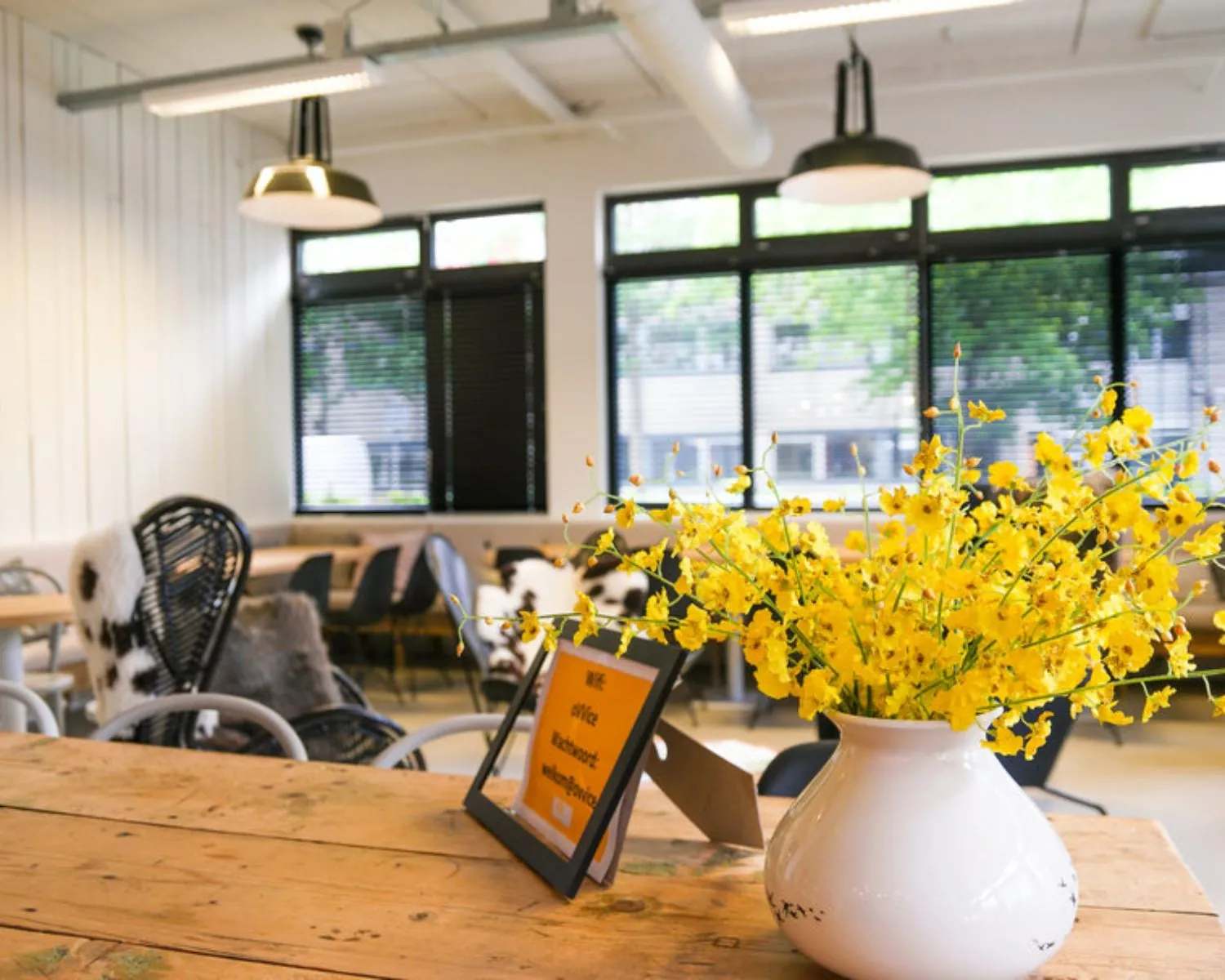 Modern ingerichte kantoorruimte aan de Hogehilweg 19 in Amsterdam met bloemenvaas en informatiebord op houten tafel.