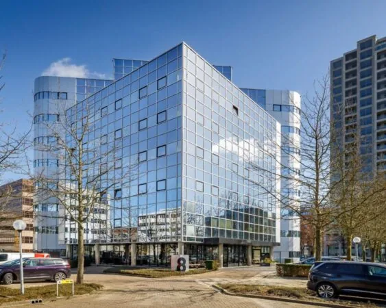 Modern kantoorgebouw met spiegelende gevel aan de Hogehilweg 8 in Amsterdam, omringd door bomen en geparkeerde auto's.