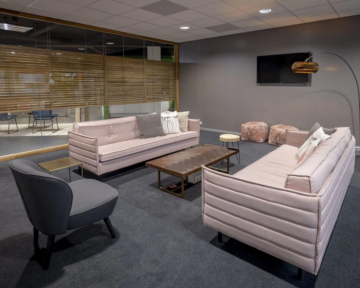 Moderne kantoorlounge in Hogehilweg 8-6 met roze banken, designmeubilair en glazen wand.