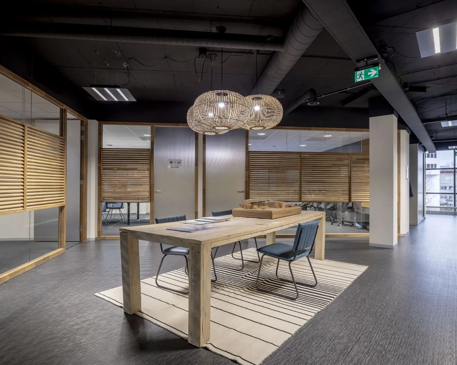 Moderne kantoorruimte aan de Hogehilweg 8 met houten vergadertafel, designlampen en glazen wanden met houten jaloezieën.