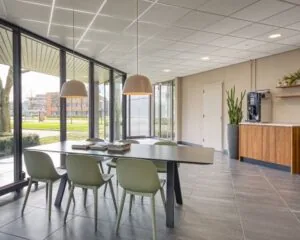 Moderne kantoorruimte met grote ramen, vergadertafel, hanglampen en een koffiehoek aan de Hullenbergweg 4 in Amsterdam.