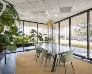Moderne kantoorruimte aan de Hullenbergweg in Amsterdam met grote raampartijen, een vergadertafel en veel groene planten.
