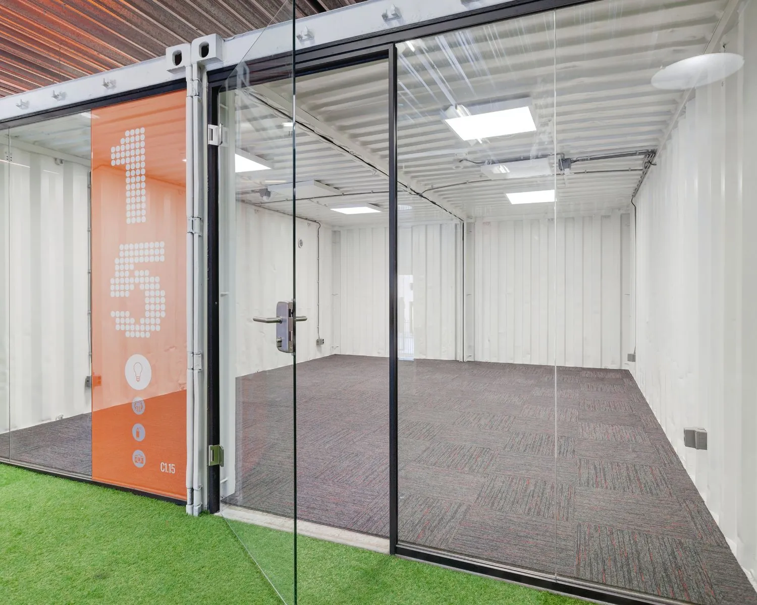 Glazen kantoorunit C1.15 in Hoofdveste 2 Houten met tapijtvloer en kunstgras buiten de entree.