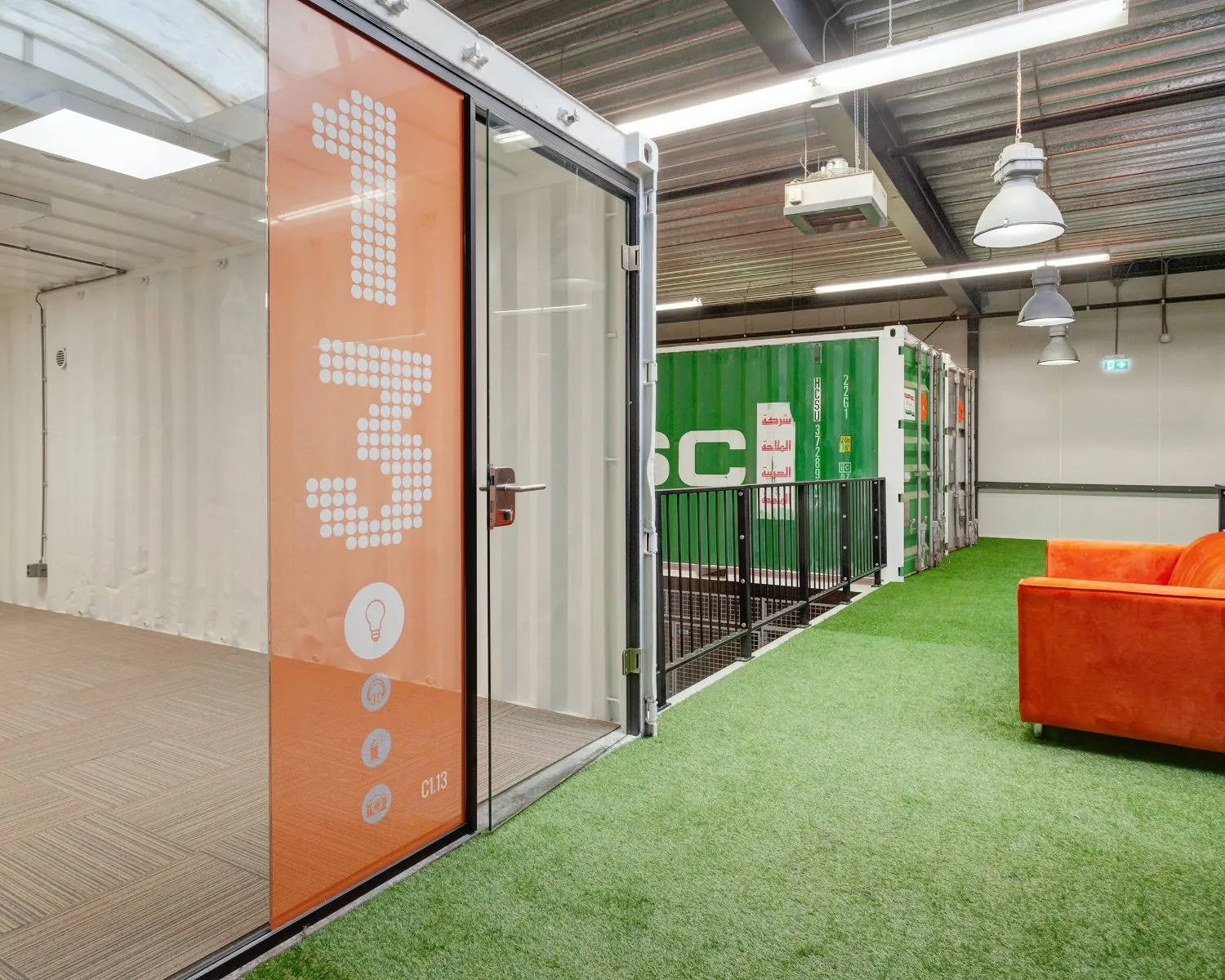Moderne kantoorruimte in Houten met unit C1.13, kunstgrasvloer en feloranje bank, ingericht in een industriële stijl met zeecontainers.