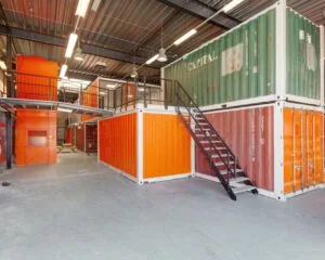 Industriële kantoorruimte in Houten opgebouwd uit gestapelde, kleurrijke zeecontainers met metalen trap en loopbrug.