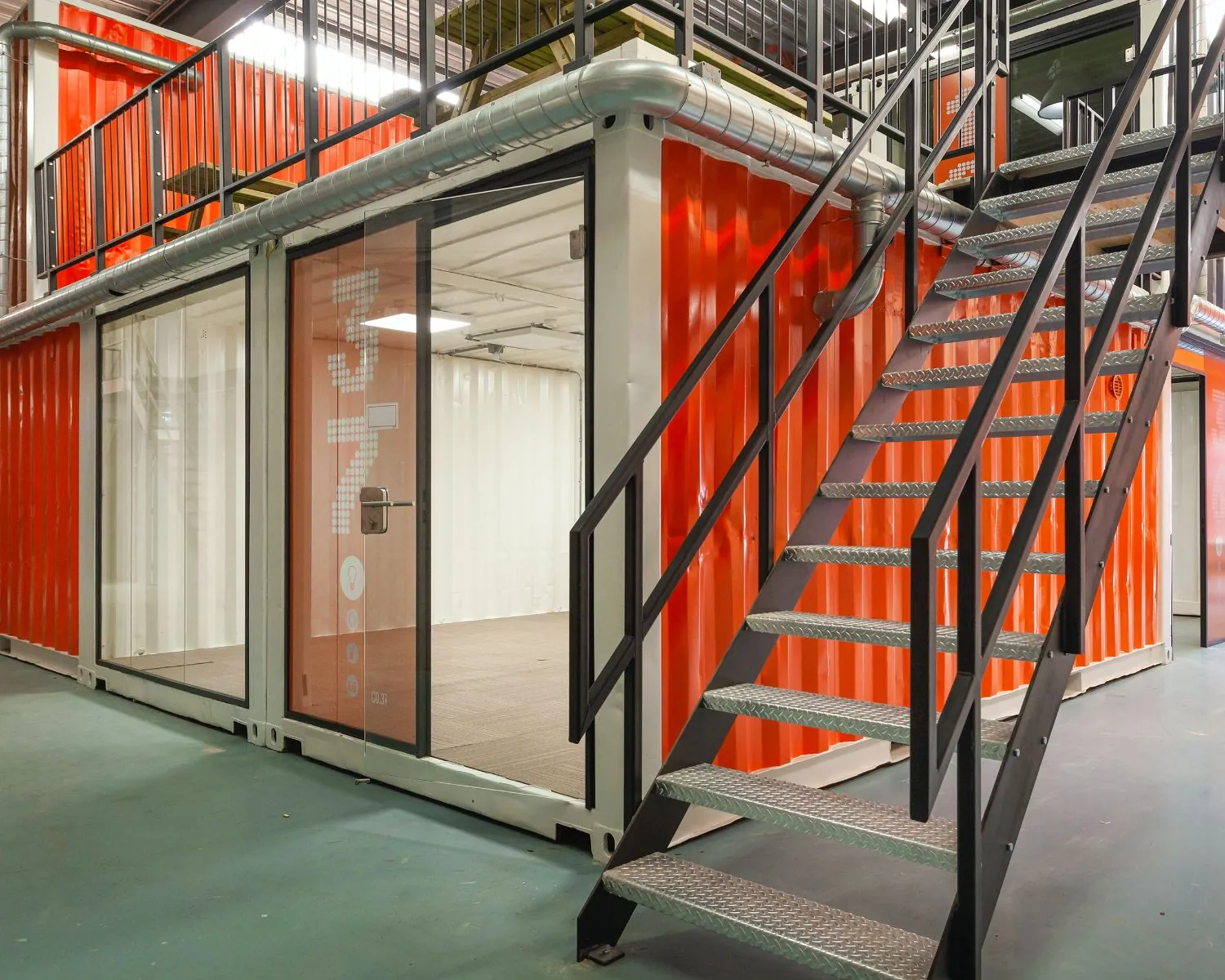 Moderne kantoorruimte in Houten, opgebouwd uit feloranje zeecontainers met metalen trap en glazen deuren.
