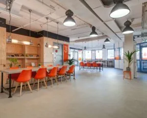 Moderne kantoorruimte aan de Innsbruckweg 130 in Rotterdam met lange tafels, oranje stoelen en industriële verlichting.
