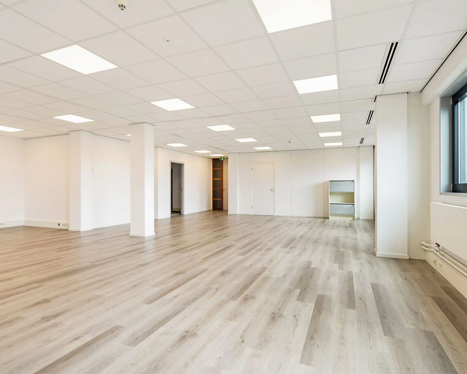 Ruime, lege kantoorruimte met licht houten vloer en systeemplafond aan de Joan Muyskenweg 40 in Amsterdam.