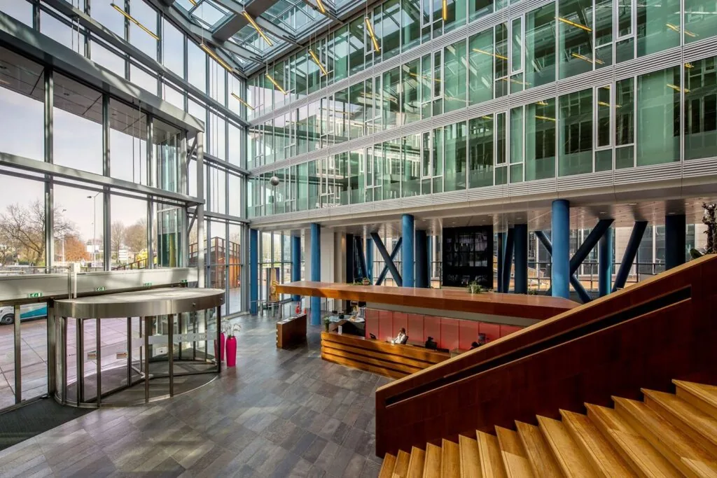 Moderne entreehal van Kennedy Tower in Eindhoven met glazen gevel, houten trap en receptiebalie.