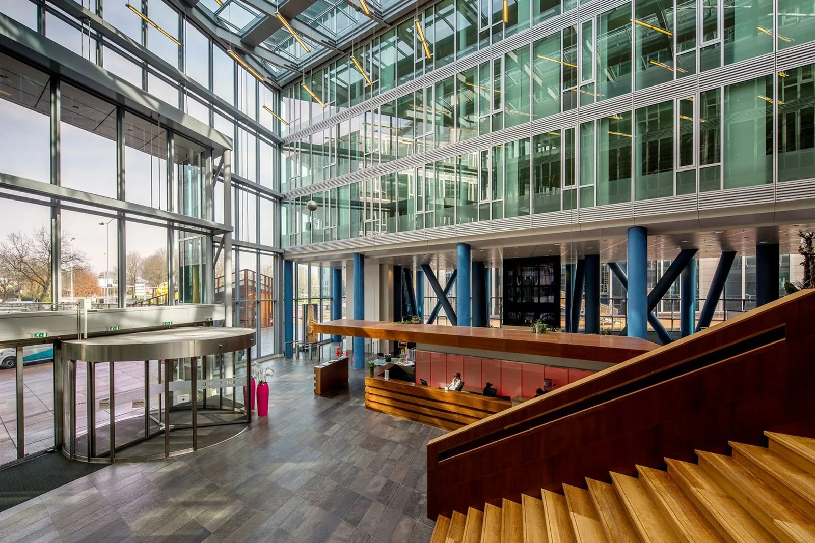 Moderne entreehal van Kennedy Tower in Eindhoven met glazen gevel, houten trap en receptiebalie.