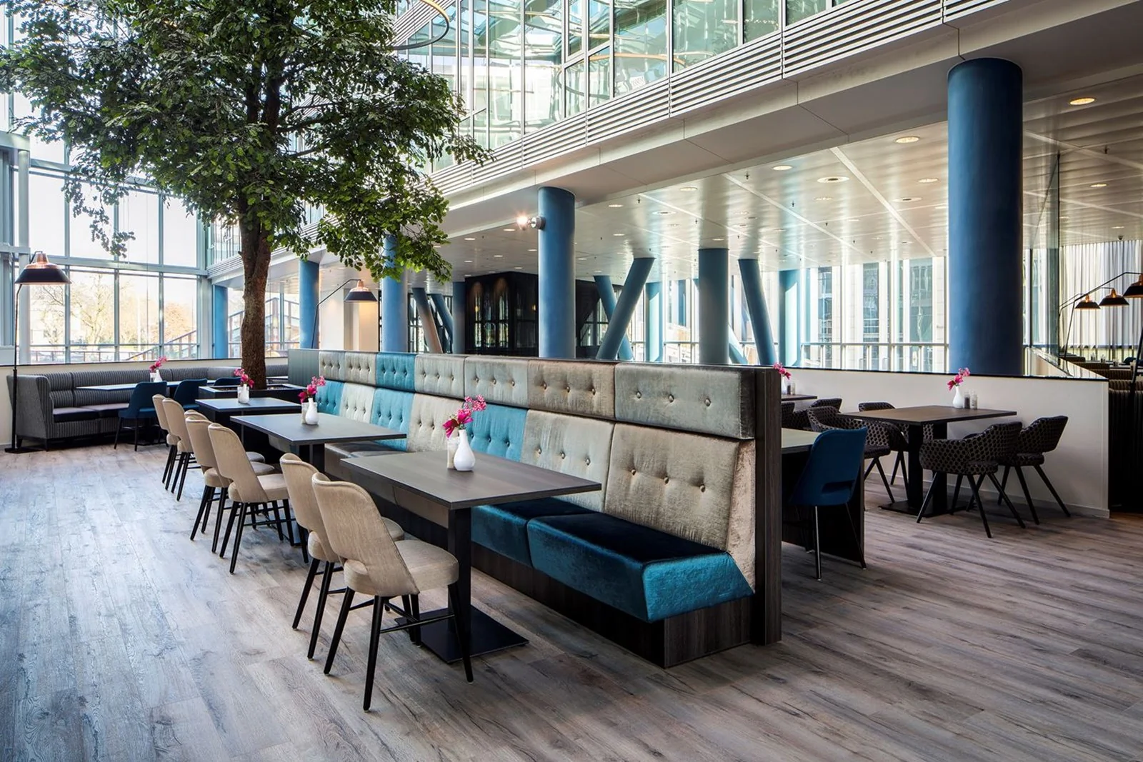 Moderne, open kantoorlounge in Kennedy Tower in Eindhoven met stijlvolle zitplekken, grote ramen en een boom als eyecatcher.