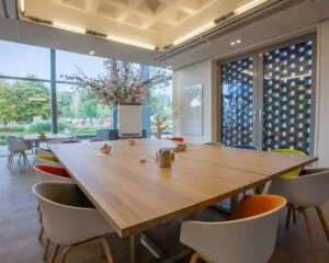 Moderne vergaderruimte met grote houten tafel, kleurrijke stoelen en uitzicht op groen bij Laan van Malkenschoten 40-4.