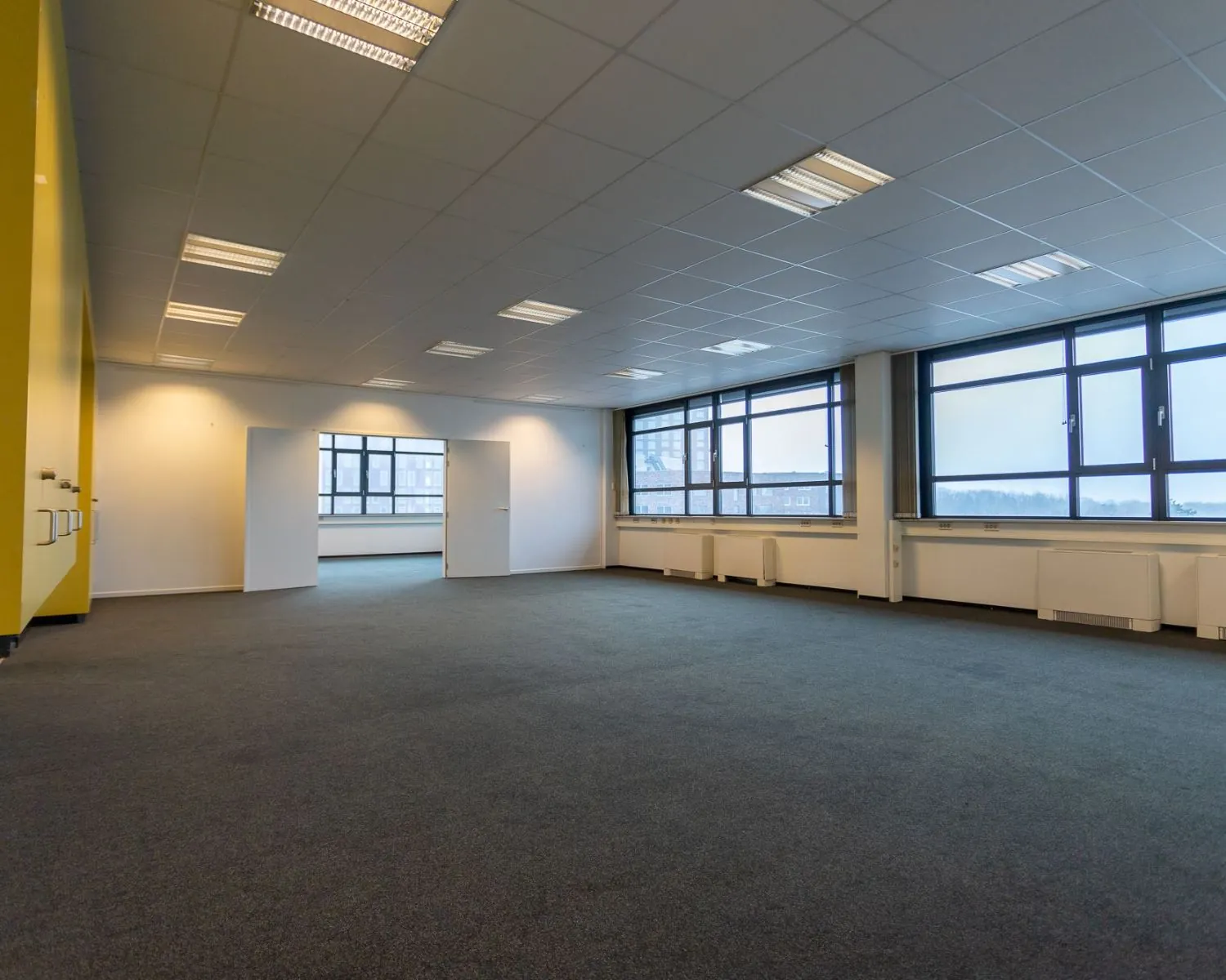 Ruime, lege kantoorruimte met tapijt en grote ramen aan de Lammenschansweg 130D.