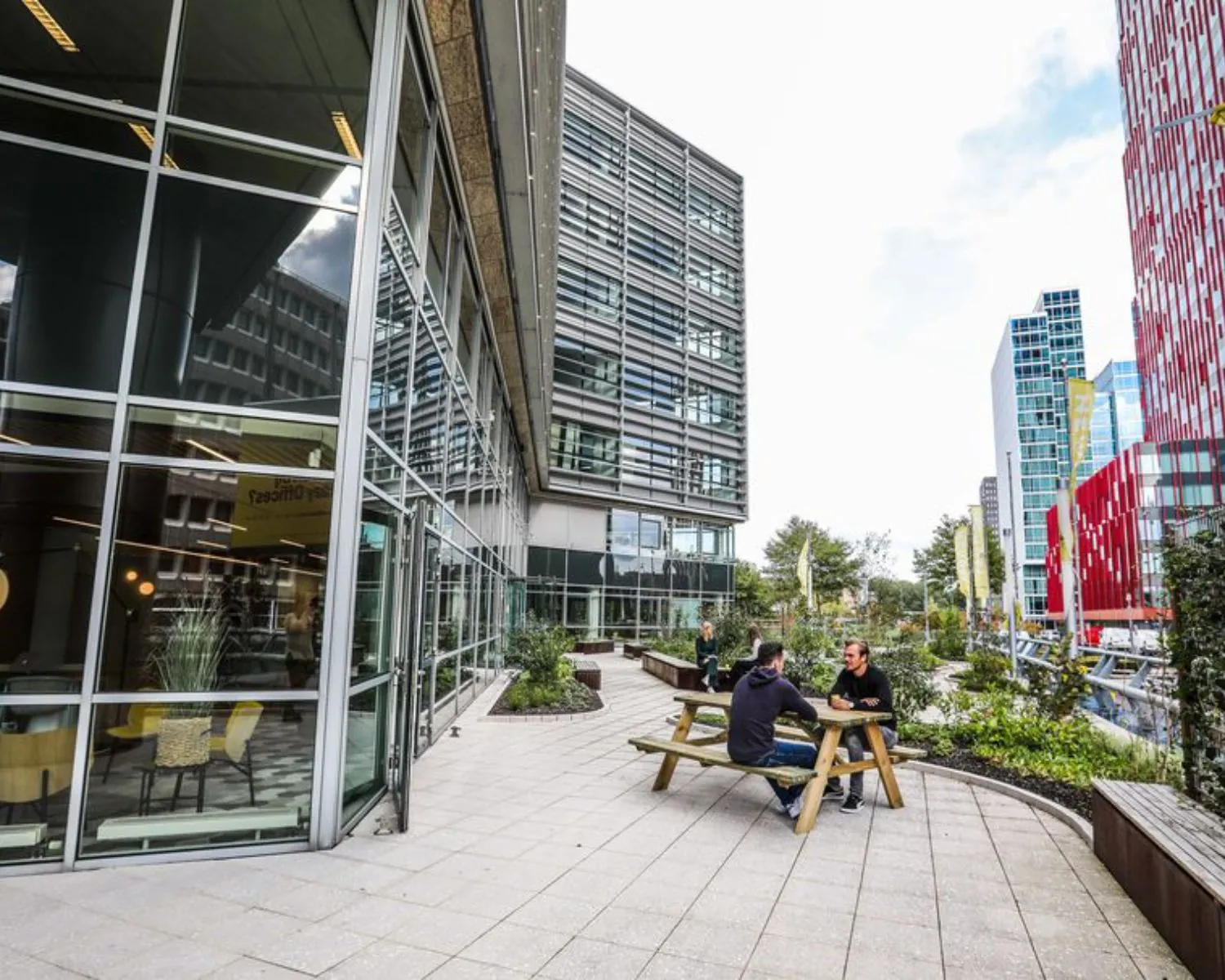 Twee mensen zitten aan een picknicktafel op het terras voor een modern kantoorgebouw aan de PJ Oudweg 41 in Almere.