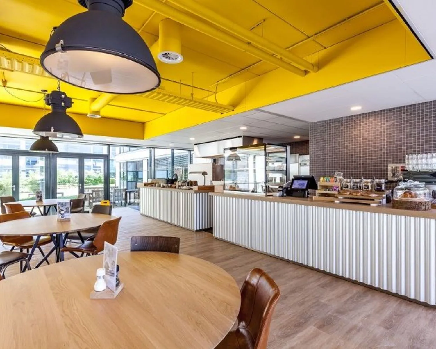 Moderne kantine met houten tafels, een koffiebar en een geel plafond in een kantoorruimte aan de Polarisavenue.