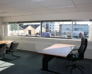 Kantoorruimte met bureaus, stoelen en grote ramen met uitzicht op bedrijventerrein aan de Pompoenweg.