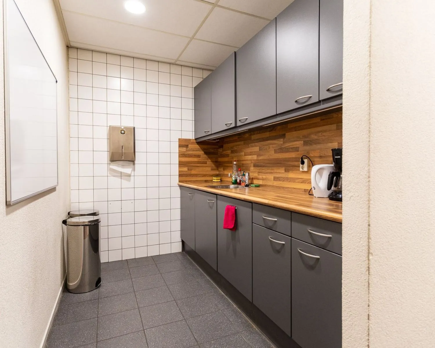 Moderne kantoorpantry aan de Pompoenweg met grijze kasten, houten werkblad en koffiezetapparaat.