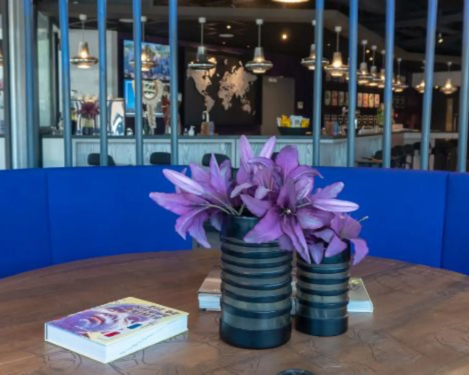 Moderne kantoorruimte met een ronde tafel, paarse bloemen in een vaas en een loungegedeelte met blauwe bank op Prins Bernhardplein 200 in Amsterdam.