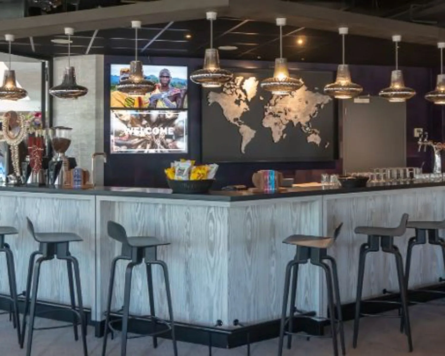 Moderne koffiebalie met barkrukken, wereldkaart aan de muur en sfeerverlichting in een kantoorruimte aan het Prins Bernhardplein 200 in Amsterdam.