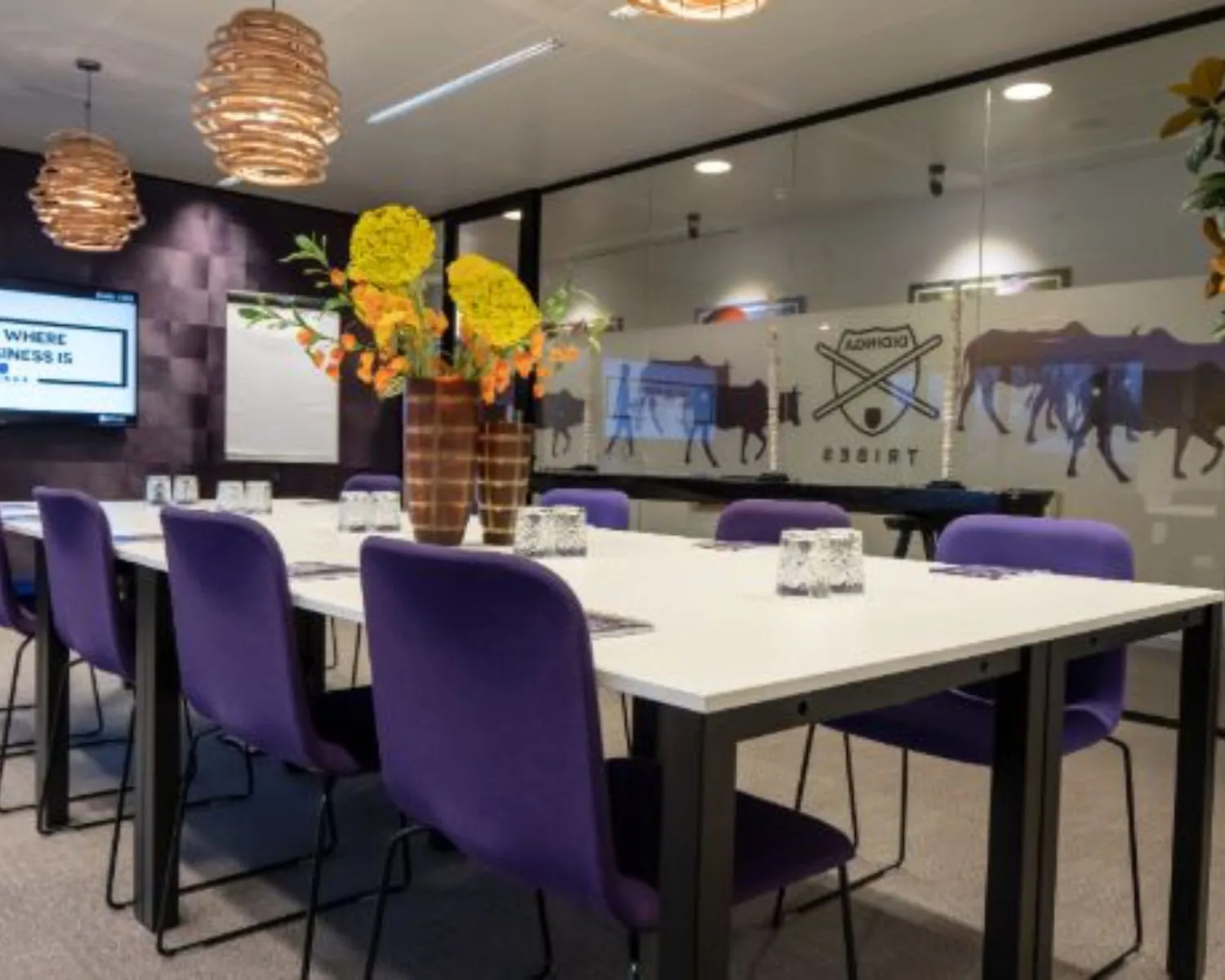 Moderne vergaderruimte met paarse stoelen, glazen wanden en decoratieve verlichting in kantoorruimte aan Prins Bernhardplein 200 in Amsterdam.