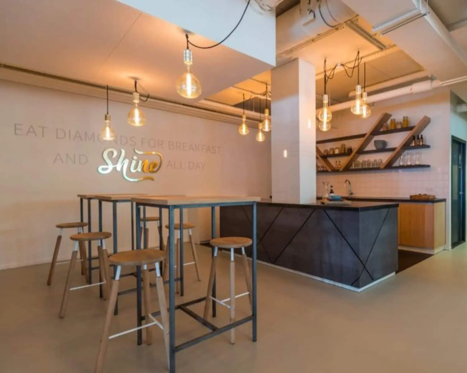 Moderne kantoorkeuken met hoge tafels, barkrukken, industriële hanglampen en decoratieve wandplanken aan de Roggestraat 111 in Apeldoorn.