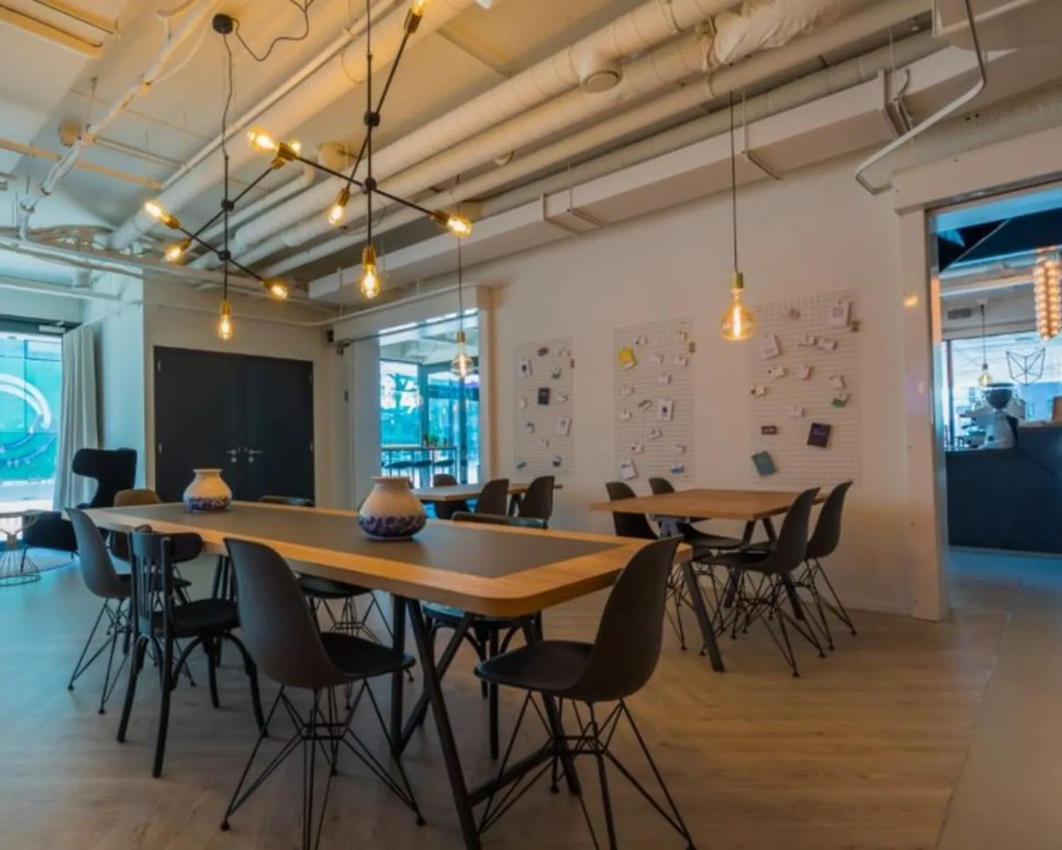 Moderne kantoorruimte aan de Roggestraat 111 in Apeldoorn met lange houten tafels, zwarte stoelen en industriële plafondverlichting.