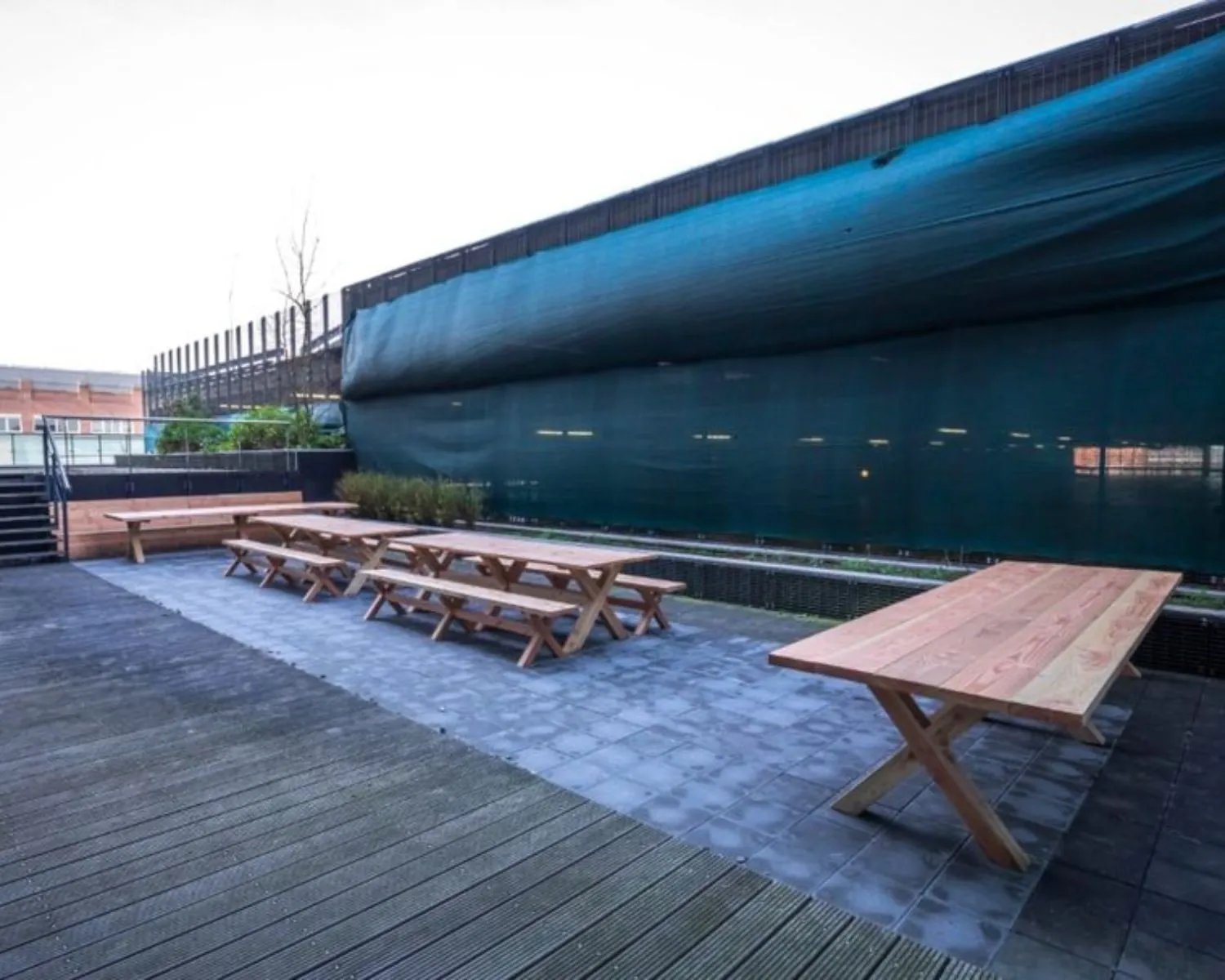 Buitenterras met meerdere houten picknicktafels bij kantoorpand aan de Roggestraat 111 in Apeldoorn.