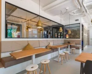 Moderne kantoorruimte in Apeldoorn met lange zitbanken, houten tafels, barkrukken en sfeervolle verlichting.