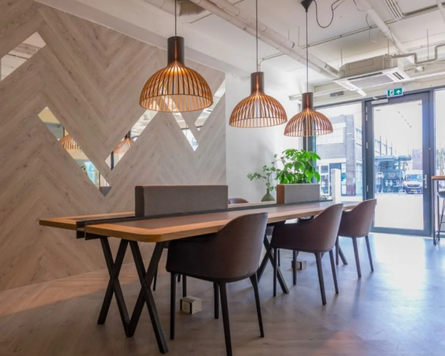 Moderne, lichte kantoorruimte aan de Roggestraat 111 in Apeldoorn met houten details, hanglampen en een lange werktafel met stoelen.