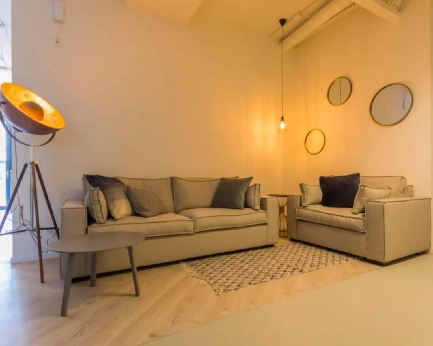 Gezellige zithoek in een kantoorruimte aan de Roggestraat 111 in Apeldoorn met twee beige banken, een vloerkleed, designlamp en ronde wandspiegels.